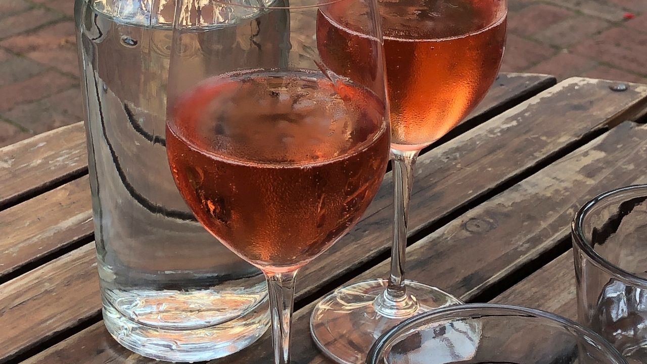 Grenache Noir Grape In Provence - two glasses of rosé with a bottle of water on a wooden table